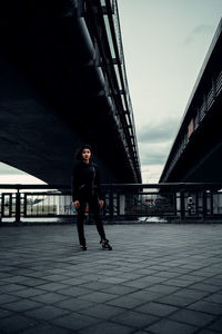 Side view of young woman on bridge against sky in city