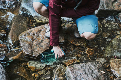 Woman taking pure water to bottle from mountain stream during trekking in mountains