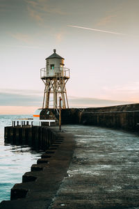 Lighthouse by sea against sky during sunset