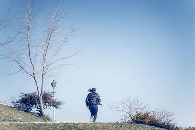 Rear view of man standing by bare tree against sky