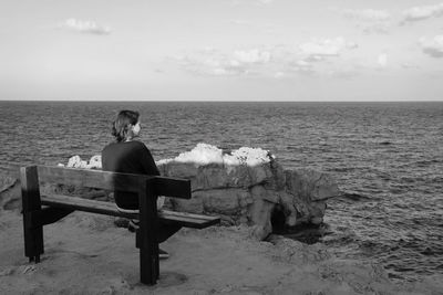 Man sitting on bench by sea against sky