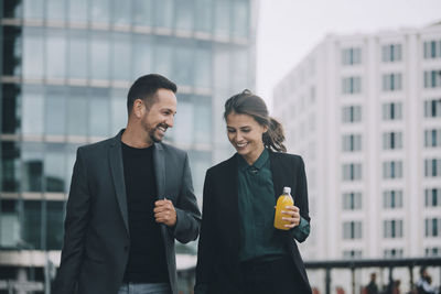 Smiling businesswoman and businessman talking while walking in city