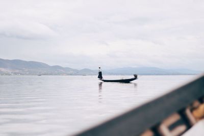 Mid distance view of woman standing in boat on sea against cloudy sky