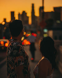 Rear view of people standing in city at sunset