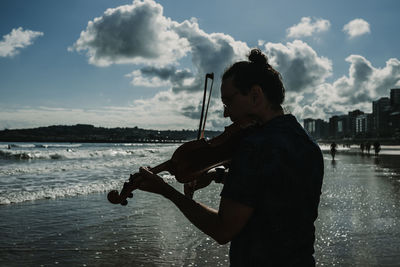 Man playing violin while standing on beach