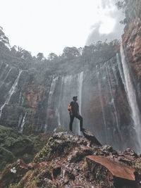 Man standing on rock against waterfall