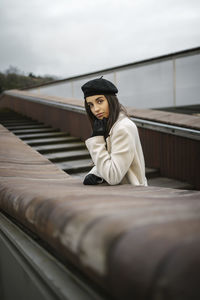 Confident woman with hand on chin leaning over retaining wall at evening