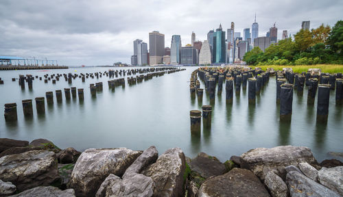 Wooden posts on river by buildings against sky