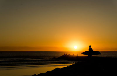 Silhouette woman standing on beach against orange sky