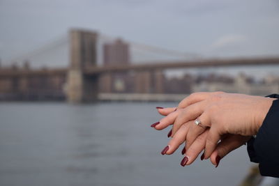 Cropped image of hand against bridge over river