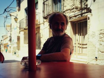 Thoughtful man sitting at sidewalk cafe against buildings in town