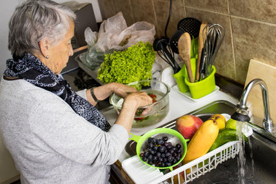 Senior woman sanding at kitchen with vegetables and fruits