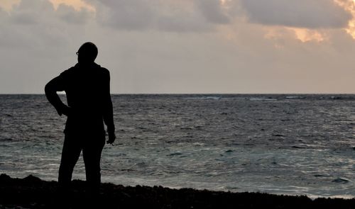 Silhouette man standing on beach against sky during sunset