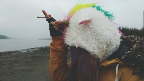 Woman holding cigarette while wearing unicorn mask