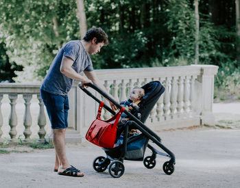 Caucasian young male dad pulls his hand to a little daughter sitting in a stroller