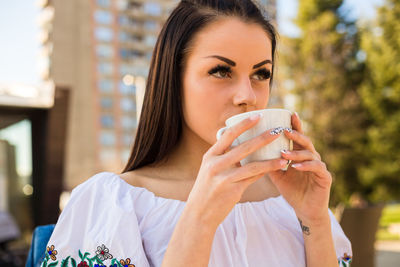 Thoughtful young woman drinking coffee while sitting at outdoor cafe in city