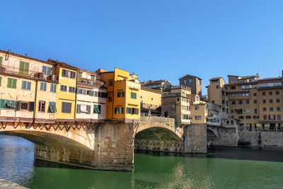 Arch bridge over river by buildings against clear blue sky