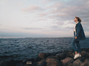 Man standing on rock by sea against sky