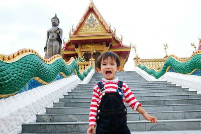 Boy standing on steps at wat baan ngao temple against clear sky