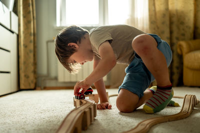 The boy is playing a toy train at home. the child is building a railway from a wooden construction 