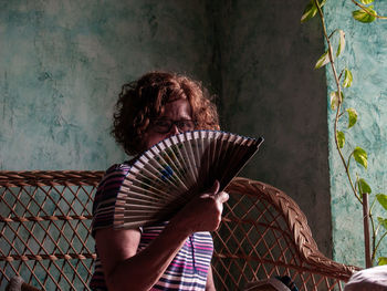 Portrait of woman covering face with hand fan at home