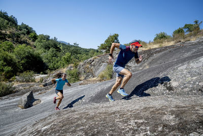 Male coach running race with female athlete on rock mountain