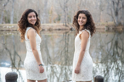 Portrait of smiling sisters wearing white dresses while standing by lake