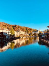 Reflection of buildings in river against clear blue sky