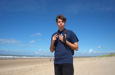 Young man standing at beach against sky