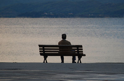 Rear view of man sitting on bench at beach
port, pyrgadikia, halkidiki, greece.