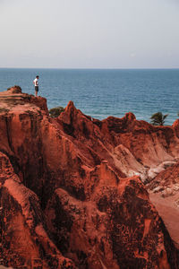 Distant view of man standing on rock formation by sea against sky