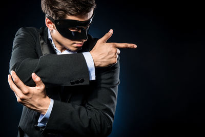 Man in mask gesturing while standing against black background