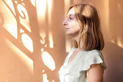 Portrait of a young woman in profile with red hair against the background of a wall with shadows 