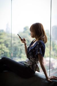 Side view of woman sitting on mobile phone