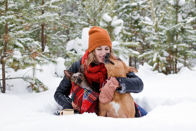 Woman with dogs on snow field against trees during winter