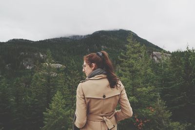 Young woman standing by tree on mountain against sky