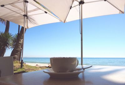 Deck chairs and table on beach against clear sky