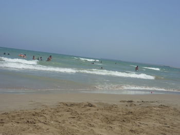 Tourists enjoying on beach against clear sky