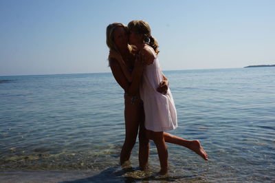 Friends enjoying while standing against sea at beach