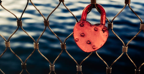 Heart-shaped red love lock hanging on a metal bridge railing