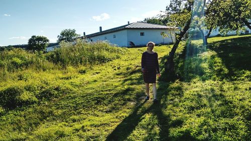 Mid adult woman walking on grassy field against sky during sunny day