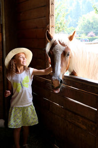 Portrait of happy little girl petting horse in barn