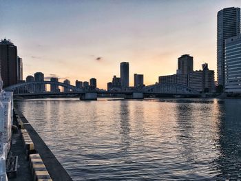 Sea by cityscape against sky during sunset