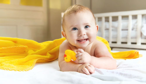 Happy baby girl with rubber duck lying on bed at home