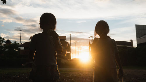 Rear view of people standing against sky during sunset