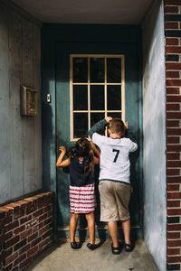 Rear view of playful siblings looking through window at home