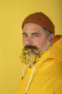 An attractive bearded man with flowers in his beard, isolated on yellow background. 
