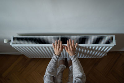 Woman in woolen sweatshirt tries to catch stream of warm air from central heater touching device
