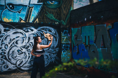 Full length of young woman standing against graffiti wall