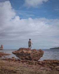 Man standing on rock by sea against sky